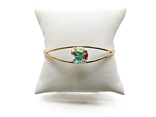 Gold bracelet with colorful gemstone on cushion.