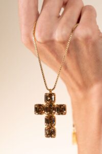 Hand holding gold brown gemstone cross pendant