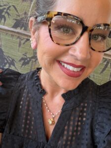 Smiling woman with tortoiseshell glasses and necklace